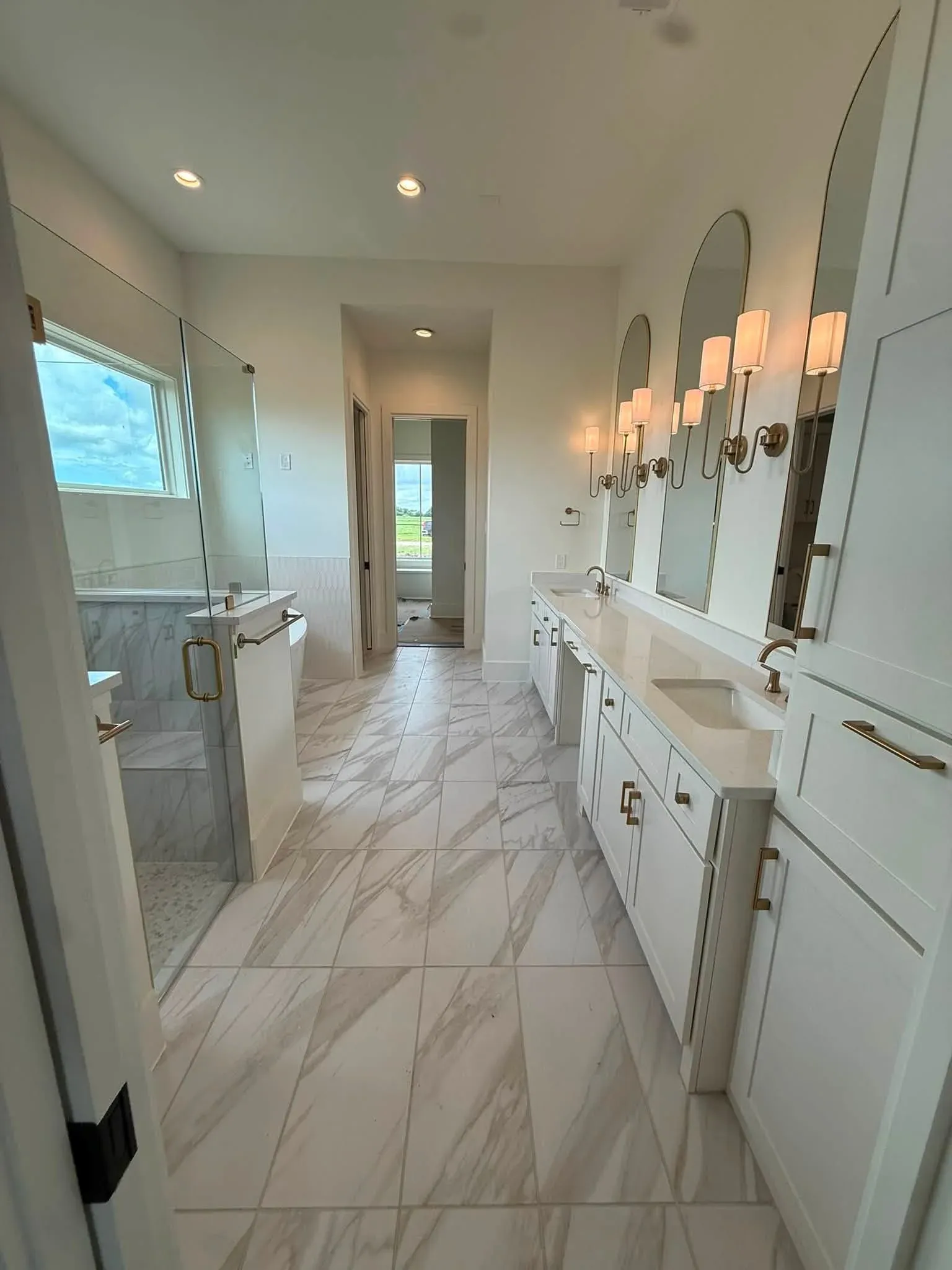 Finished double vanity suite with marble-look flooring, custom mirrors, and brass lighting