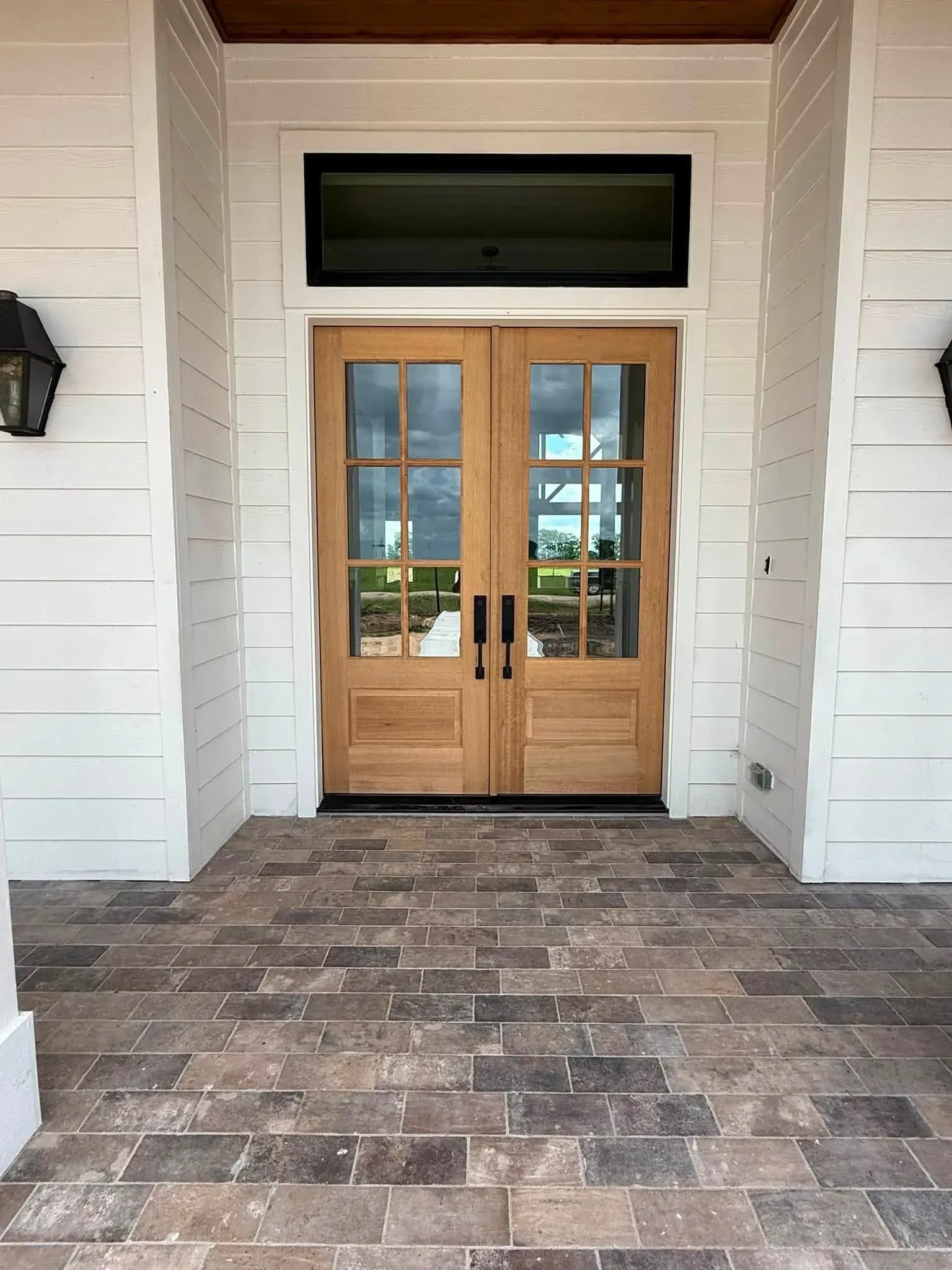 Finished covered entry with tumbled stone tile and natural wood double doors