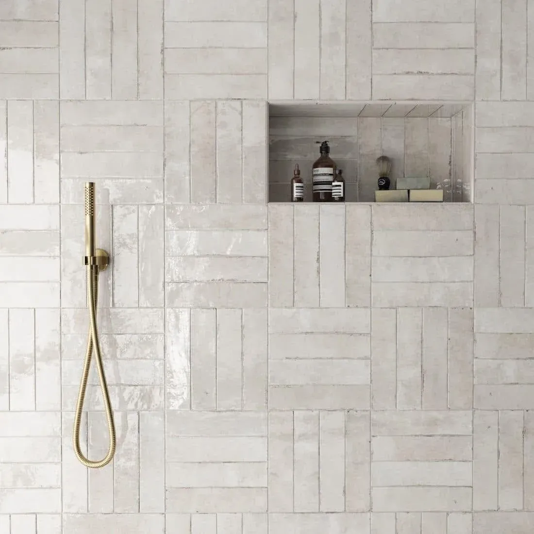 Finished white artisan tile shower wall with a recessed niche and brass hand shower