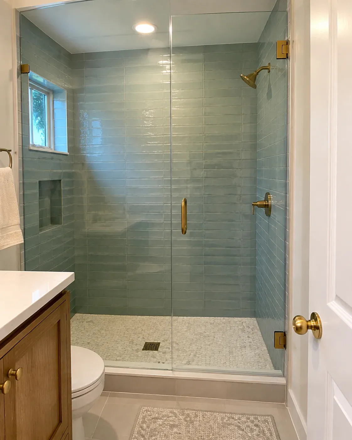 Selection concept showing a finished shower with blue-green glazed wall tile and ivory pebble mosaic flooring